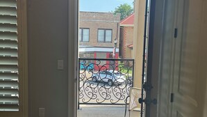 A room with a door leading to a balcony, a window with blinds, and a patterned rug on the floor. - Marr Building North Condo, Downtown Denison, Denison, Texas, Lake Texoma (Denison)