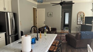 A modern kitchen with a marble island, bar stools, a refrigerator, and pendant lighting. - Marr Building North Condo, Downtown Denison, Denison, Texas, Lake Texoma (Denison)