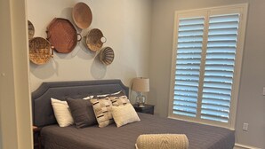 A bedroom with a bed, bedside table, lamp, wall decorations, and a window with blinds. - Marr Building North Condo, Downtown Denison, Denison, Texas, Lake Texoma (Denison)