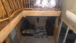 Quarto no estilo loft com estrutura de madeira, um candelabro, um banquinho revestido de pele e uma pequena mesa.