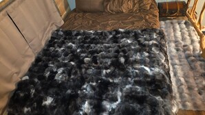Uma cama com cabeceira marrom, manta marrom e um cobertor escuro e fofinho.