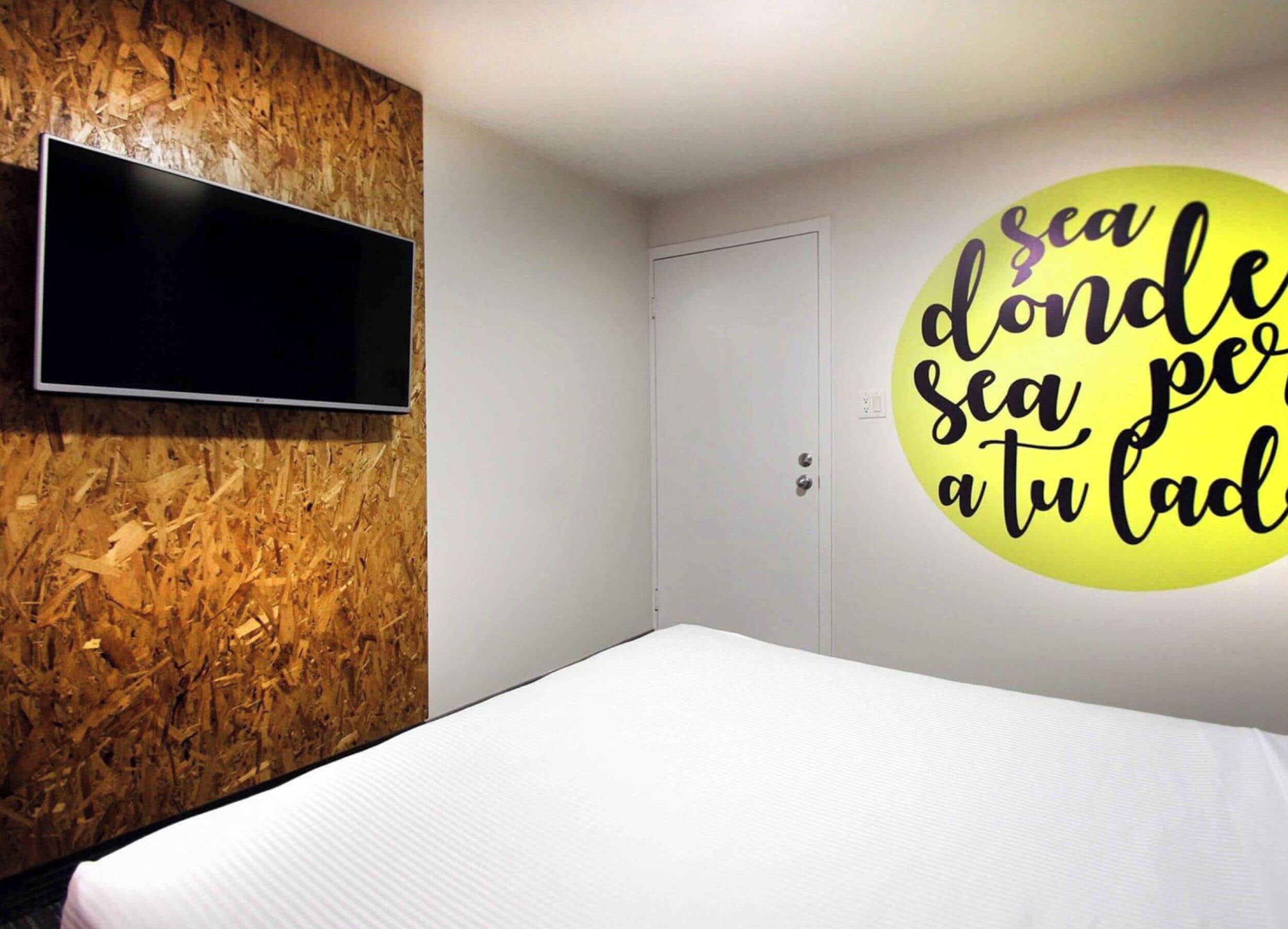 Un dormitorio con cama, televisión instalada en una pared de madera y una puerta.