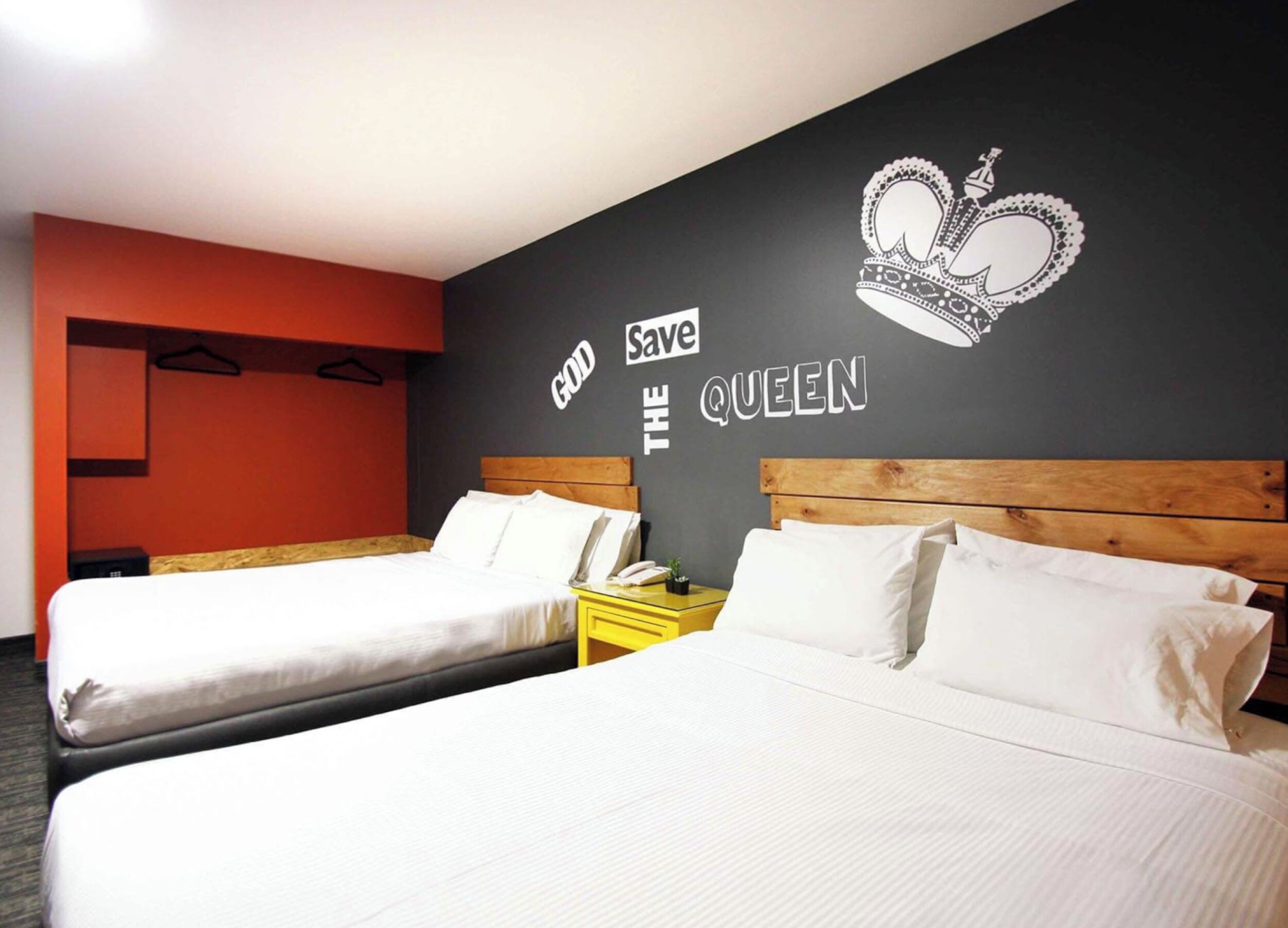 Quarto de hotel com duas camas, parede preta com coroa e texto, e uma parede em destaque na cor vermelha.