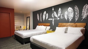 Habitación de hotel con dos camas, cabecero de madera, pared con diseños de plumas, una mesita y una silla.