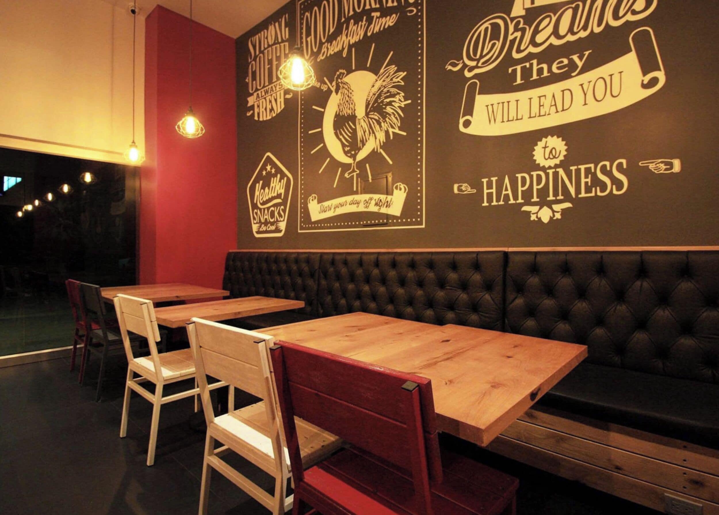A restaurant interior with wooden tables and chairs, a red accent wall, and motivational wall art.