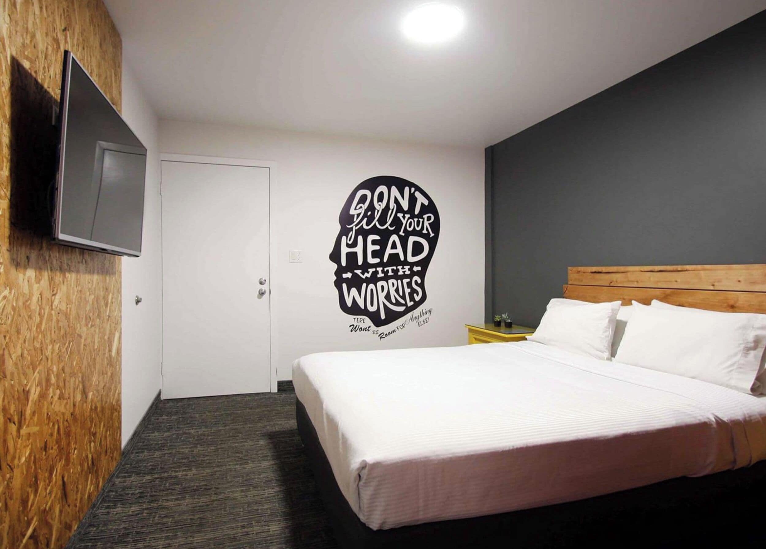A bedroom with a bed, a wall-mounted TV, a door, and a motivational quote on the wall.