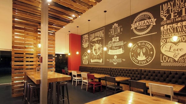 Interior de restaurante con paredes de listones de madera, varias mesas y una pared con citas inspiradoras.