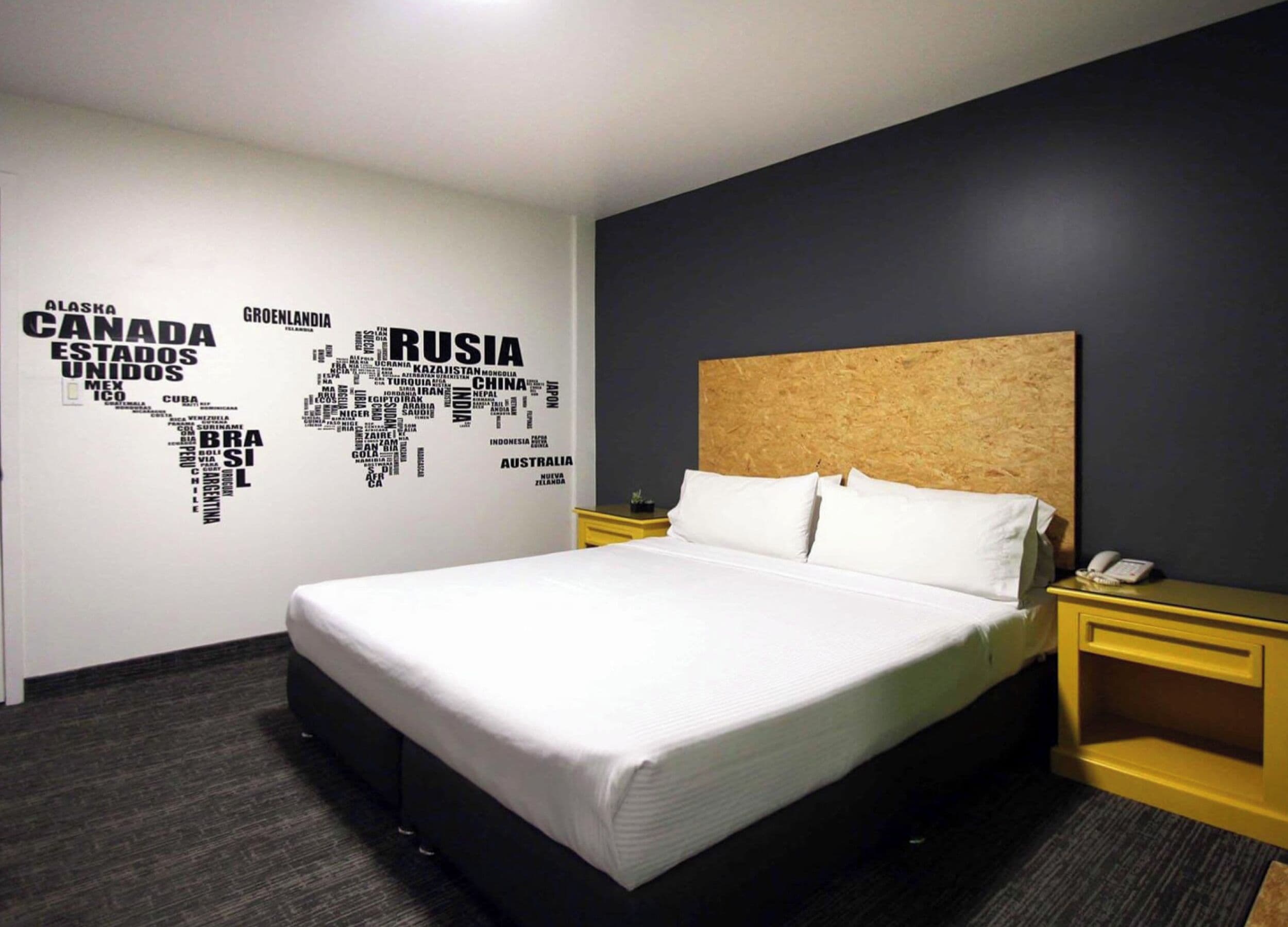 Une chambre d’hôtel avec un lit, une tête de lit, une carte géographique accrochée au mur et un téléphone sur une table de chevet.