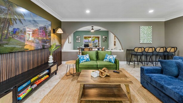 Ein Wohnzimmer mit einem grünen Sofa, einem blauen Sofa, einem Holztisch und einem Fernseher auf einem Holzgestell.