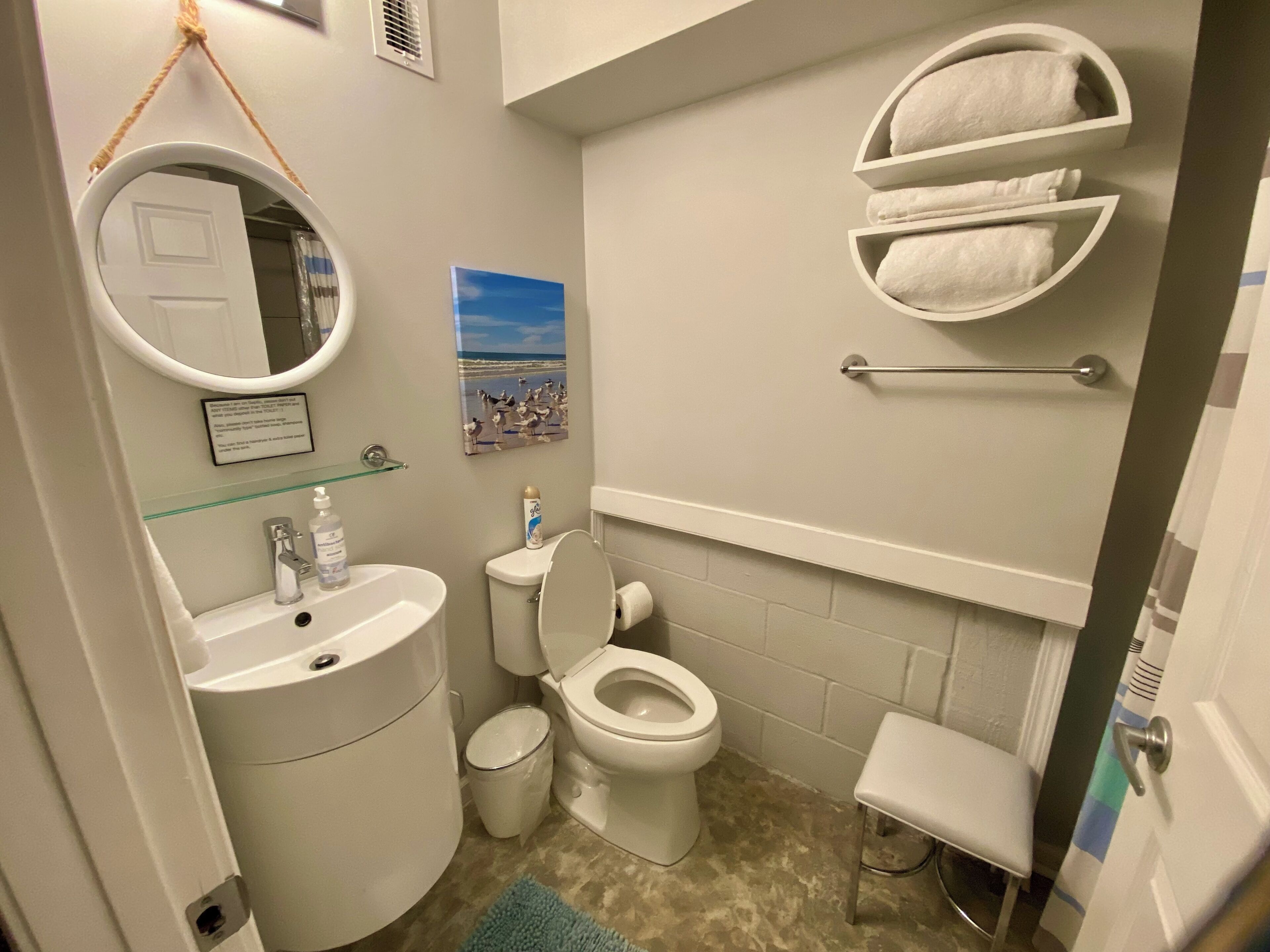A bathroom with a toilet, sink, and a glass shelf with toiletries.