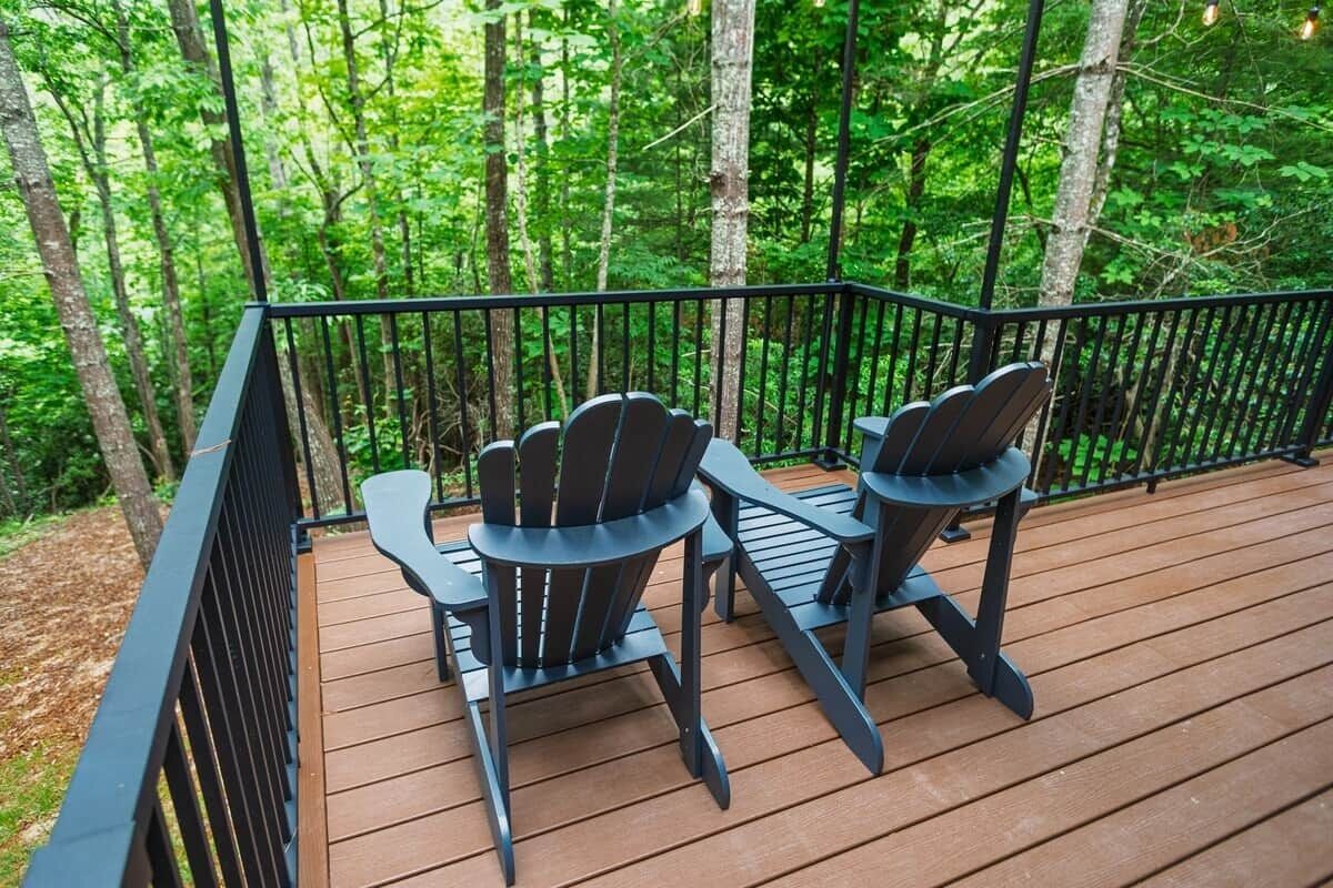 A wooden deck with two Adirondack chairs and a black metal railing.