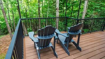 A wooden deck with two Adirondack chairs and a black metal railing.