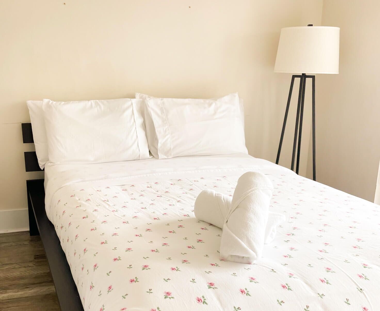 Ein ordentlich gemachtes Bett mit einer blumigen Tagesdecke, einem weißen Kopfkissen und einem gefalteten Handtuch.