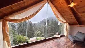 A room with a large window, wooden flooring, a sofa, and a table with a decorative item. - INARI · Meraki Cabañas & Glamping by GEstores (Mineral del Chico)