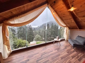 Ein Zimmer mit großem Fenster, Holzboden, einer Couch und einem Tisch mit einem dekorativen Gegenstand.