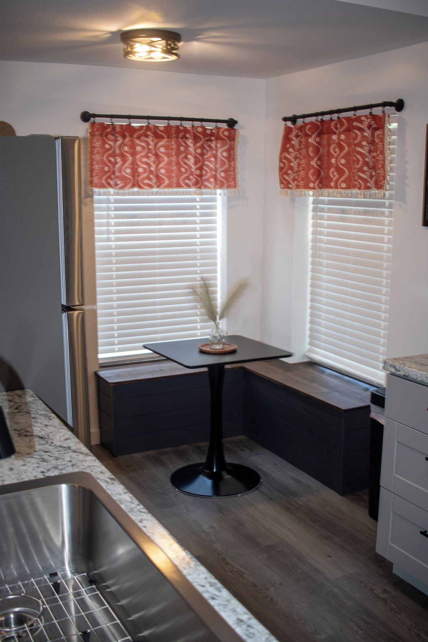 A compact kitchen with a built-in refrigerator, a sink, and a small table with a vase.