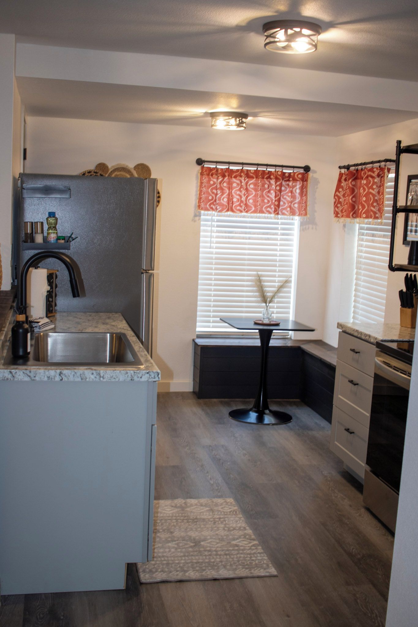 A compact kitchen with a built-in refrigerator, a sink, a small dining table, and a window with blinds.