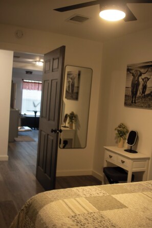 Een slaapkamer met een bed, een kaptafel, een spiegel en een deur naar een andere kamer.