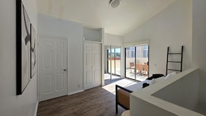 A hallway with a wooden floor, white walls, and a staircase leading to a balcony with a table and chairs.