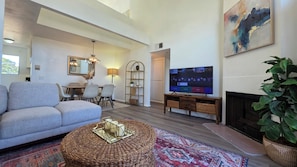 A modern living room with a sofa, TV, fireplace, and a dining area with chairs and a table.