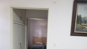 Ein Zimmer mit einem Bett, einem Kleiderschrank, einem kleinen Tisch und einem Bild an der Wand.