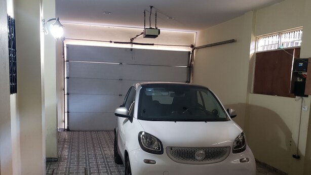 Ein weißes Auto steht in einer Garage mit gemusterten Bodenfliesen und einer geschlossenen Garagentür.