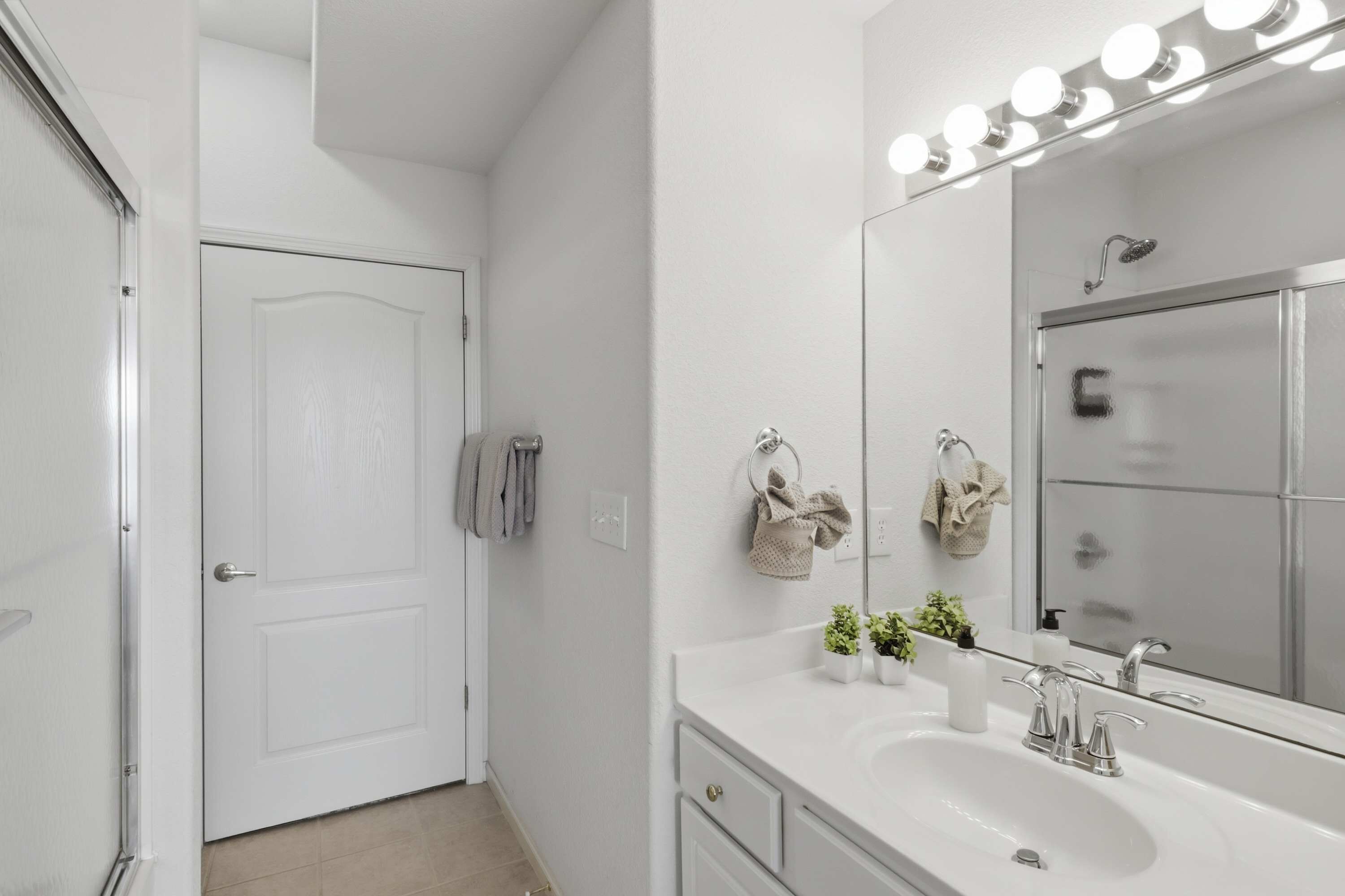 A modern bathroom with a white sink, a mirror with lights, and a shower.