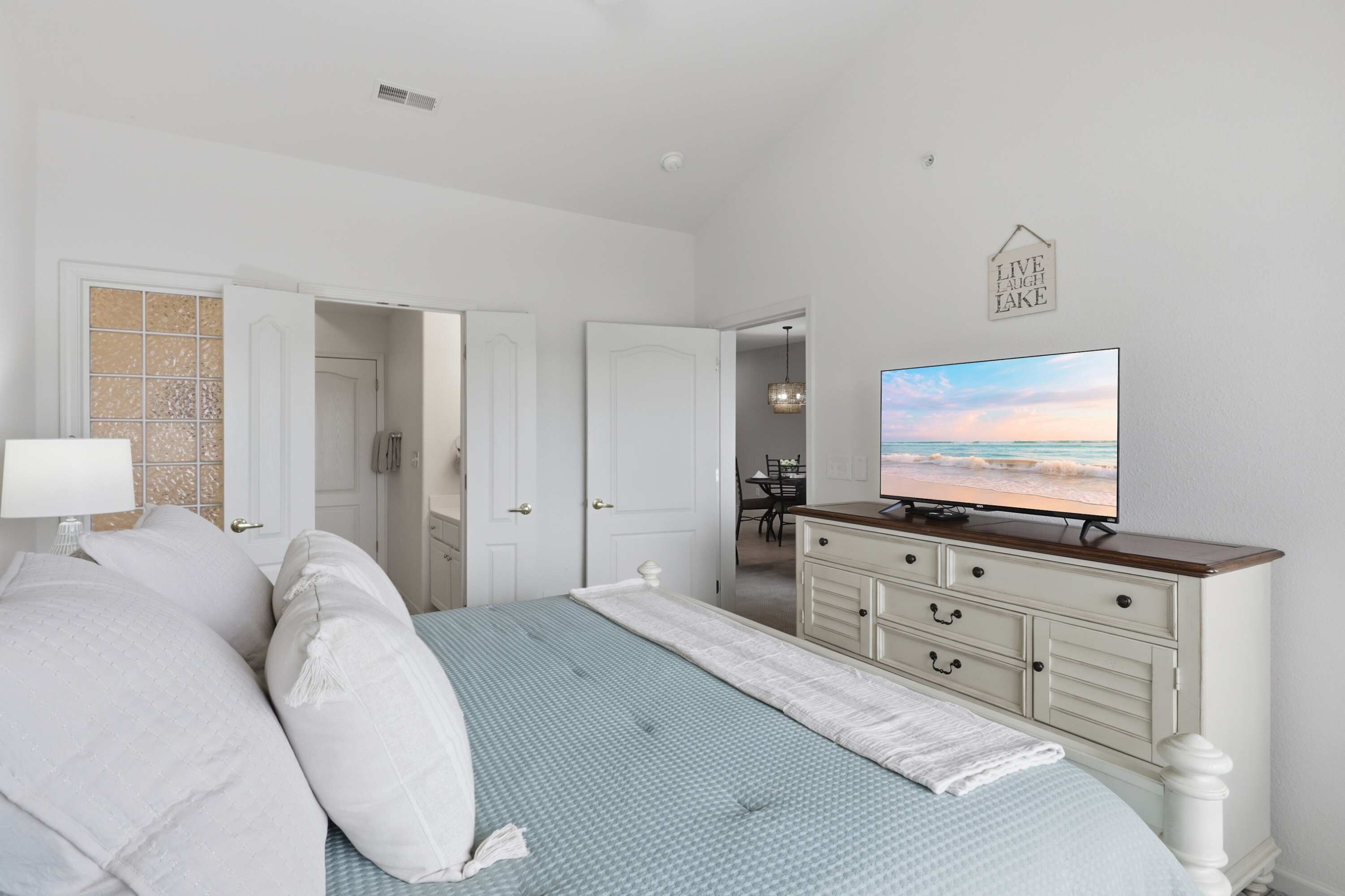 Quarto com cama, televisão, cômoda e porta que dá para outro espaço.