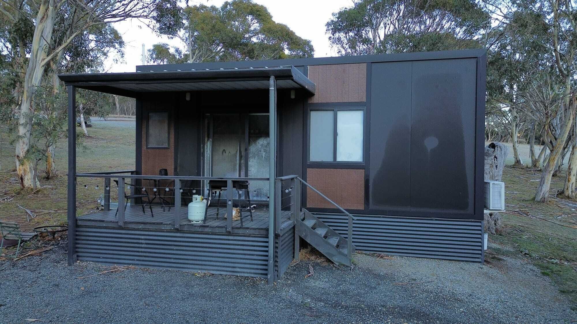 A small, modern building with a covered outdoor area, a staircase, and a window.