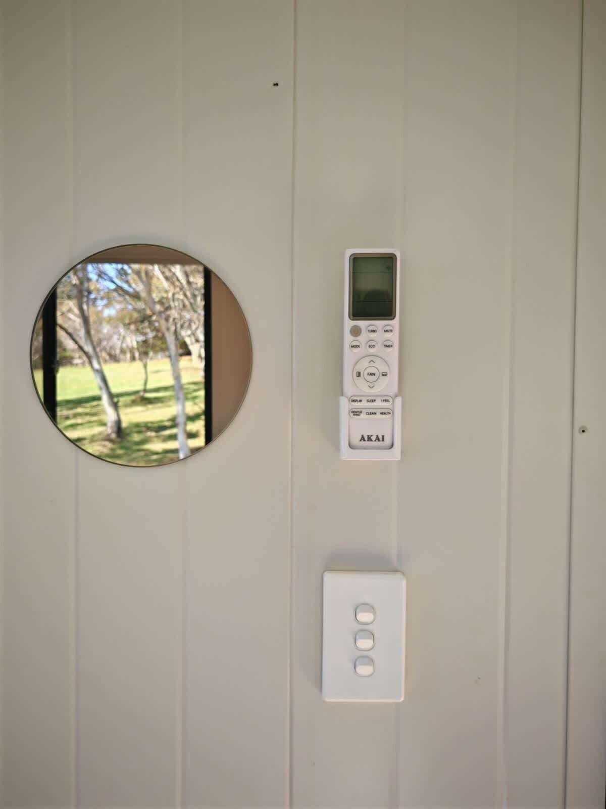 Un panel de control instalado en la pared con un espejo circular, una pantalla digital y varios botones.
