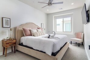 A bedroom with a bed, bedside table, lamp, chair, and a TV mounted on the wall.