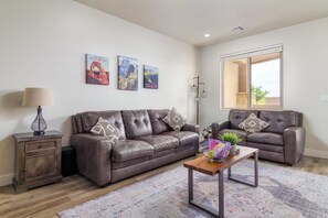 Ein Wohnzimmer mit zwei Ledersofas, einem Holztisch, einem Teppich mit Muster und Wandbildern.