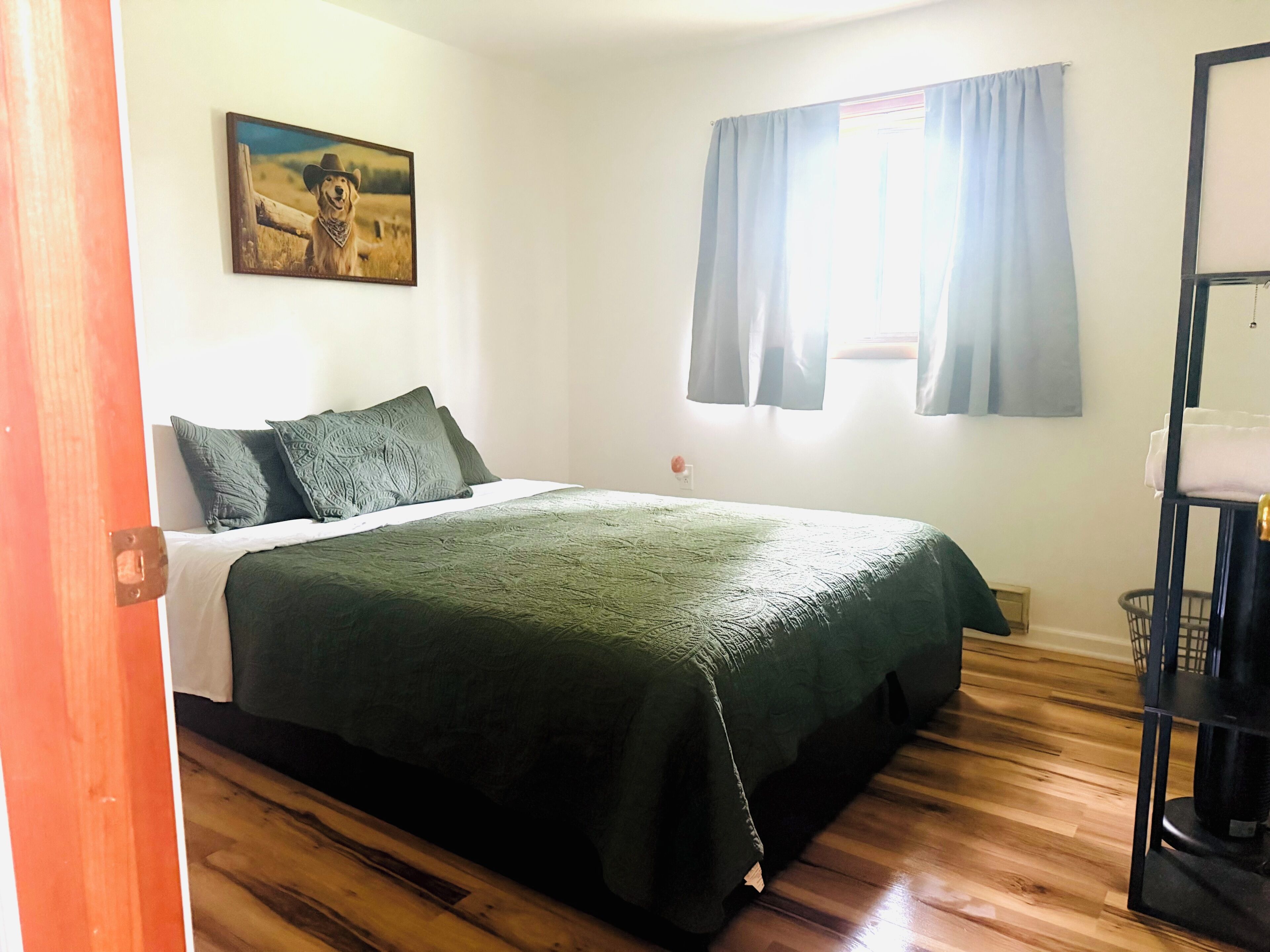 A bedroom with a bed, a painting, a window with curtains, and a wooden floor.