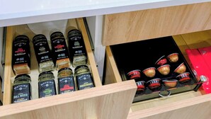 A kitchen counter with a Breville coffee maker, a Smeg mug, and a drawer with various Watkins condiments.