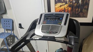 A stationary bike with a digital display, a blue chair, and a rug.