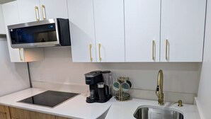 A modern kitchen with white cabinets, a built-in microwave, a coffee maker, and a stainless steel sink.