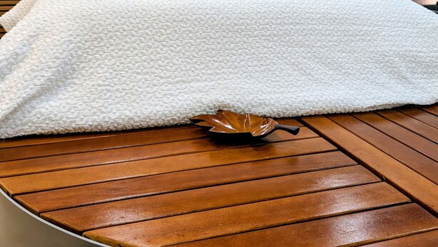 A bed with a white textured cover, wooden headboard, and a wooden table in front.