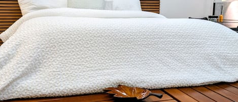 Ein Bett mit weißer Strukturdecke, einem hölzernen Kopfteil und einem Holztisch davor.