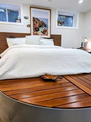 A bed with a white textured cover, wooden headboard, and a wooden table in front. - Deluxe Studio Apartment - Private Kitchen & Bath (Kitchener)