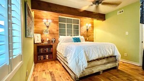 A bedroom with a wooden bed, a ceiling fan, a window with blinds, and a bookshelf. - Surf Shack - Half a block from the Ocean! (South Padre Island)