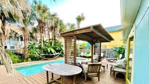 A wooden deck with a pool, outdoor furniture, and a covered seating area. - Surf Shack - Half a block from the Ocean! (South Padre Island)