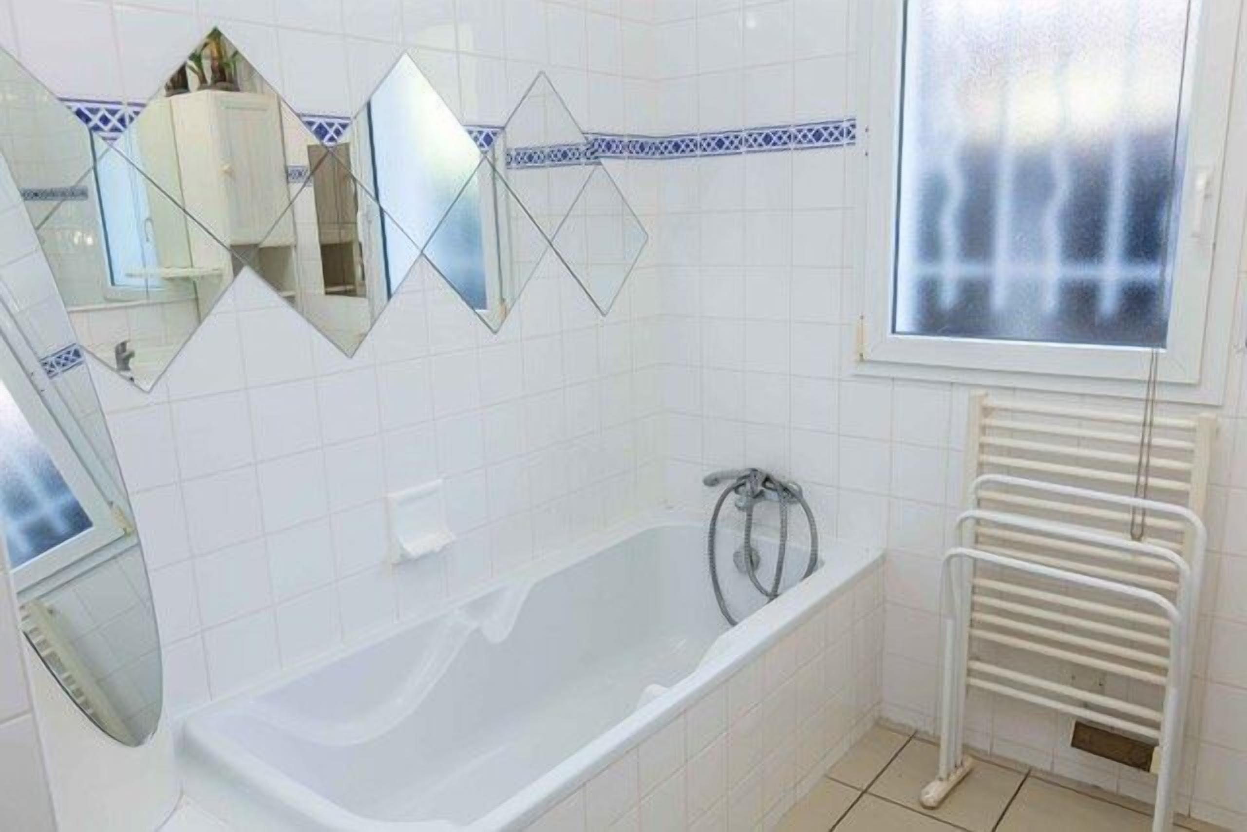 Ein Badezimmer mit einer Badewanne, Spiegeln, einem Fenster und einem Handtuchhalter.