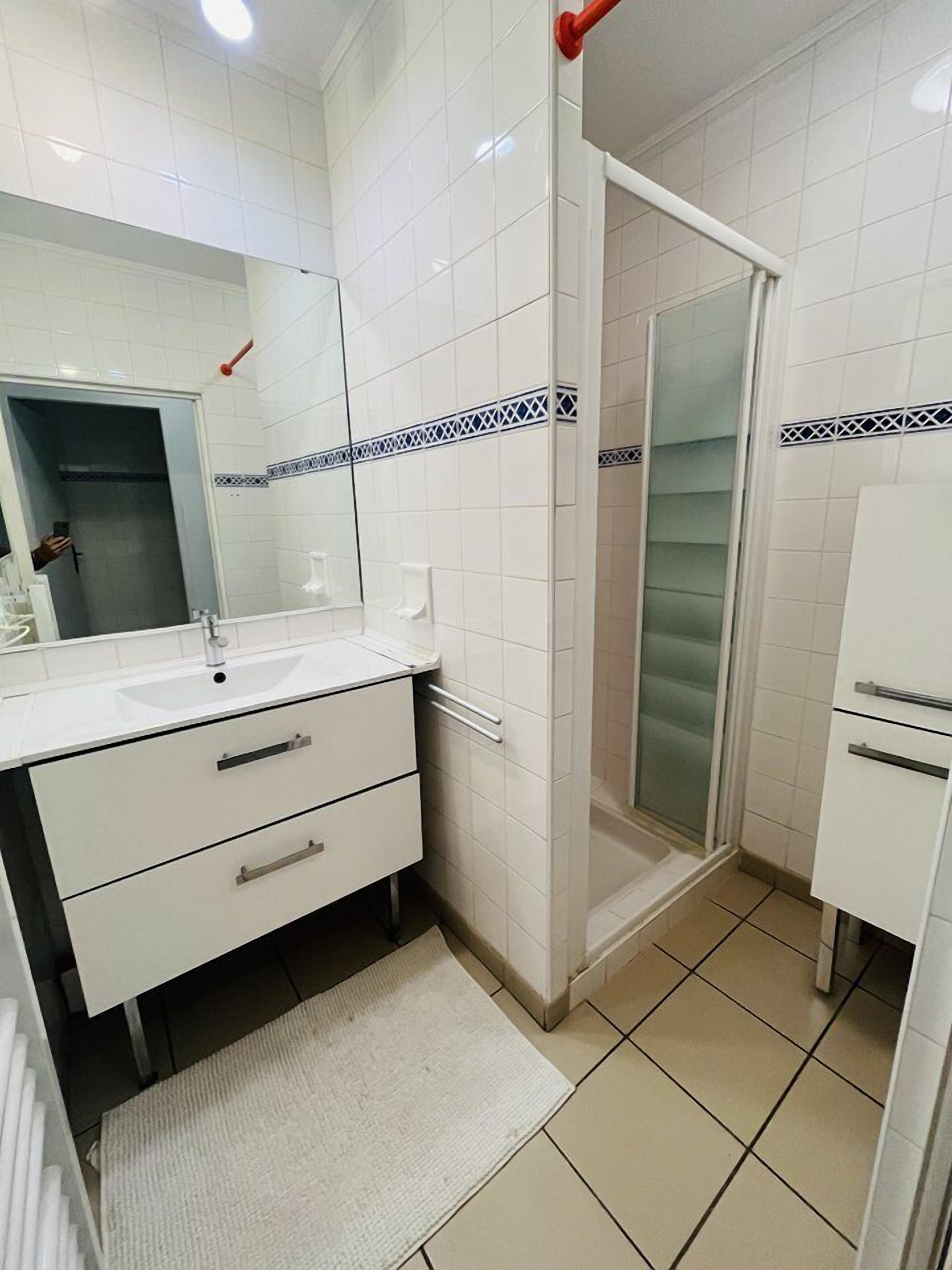 Un baño con azulejos blancos, un lavabo, un espejo, una ducha y un inodoro.