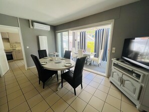 Ein Essbereich mit rundem Tisch, Stühlen, einem Fernseher und einer Küche im Hintergrund.
