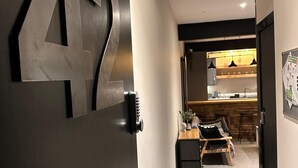 Un couloir avec une porte portant le numéro « 42 », un coin cuisine avec des tabourets de bar et un petit espace salon avec une table et des chaises.