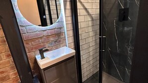 Une salle de bain moderne avec un lavabo en marbre, une douche en verre et un mur d’accent en briques.