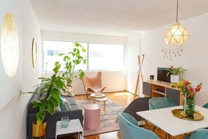 En moderne stue med sofa, spisebord, stole, fjernsyn og et stort vindue.
