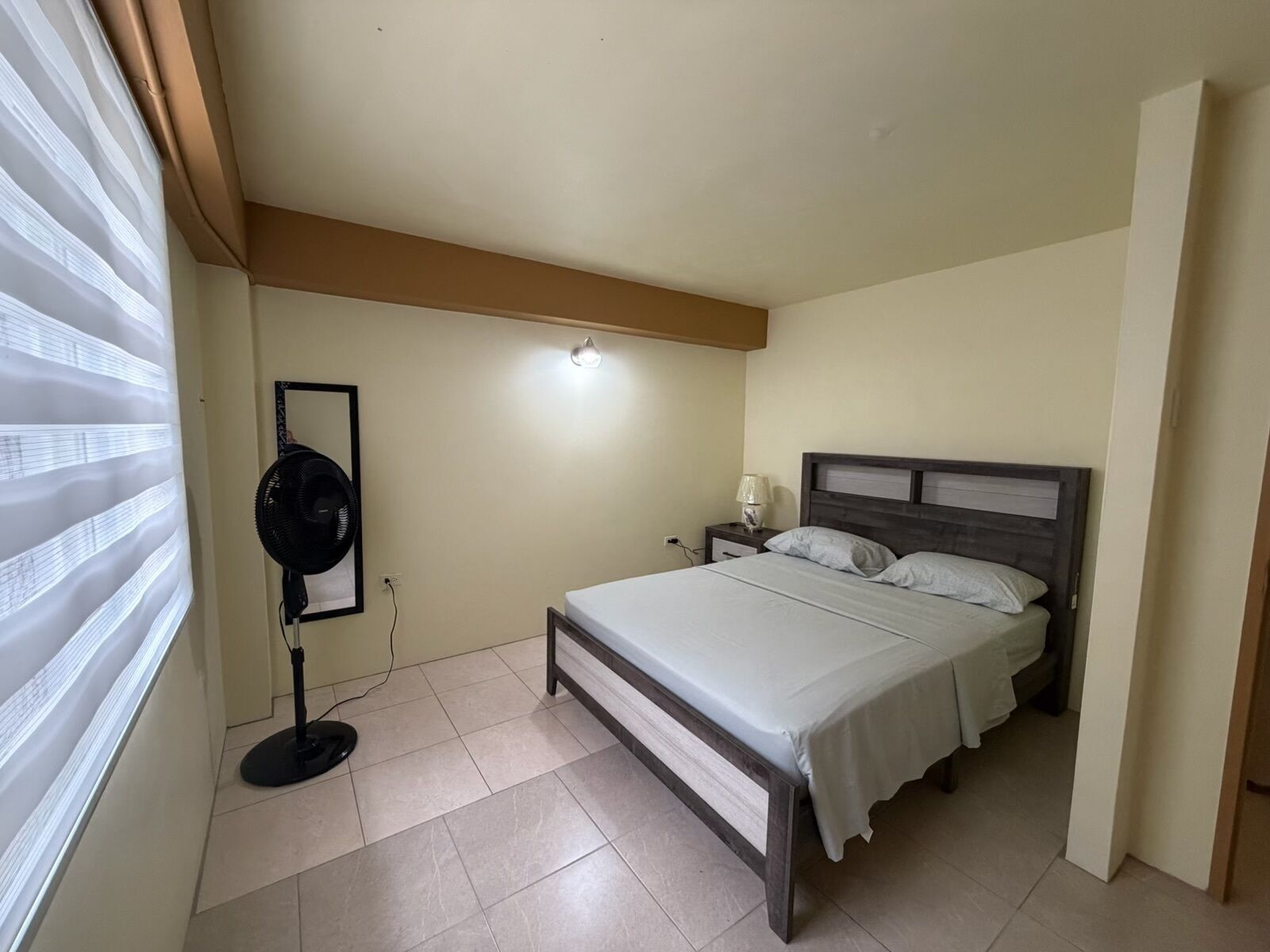 A bedroom with a bed, bedside tables, a fan, and a mirror.
