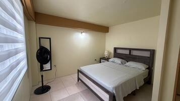 A bedroom with a bed, bedside tables, a fan, and a mirror.