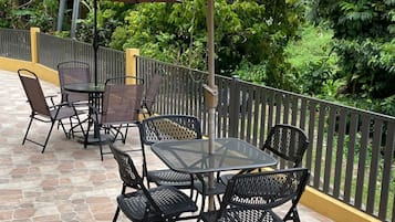 Eine Terrasse im Freien mit Steinplattenböden, Metalltischen und -stühlen sowie zwei Sonnenschirmen, die Schatten spenden.